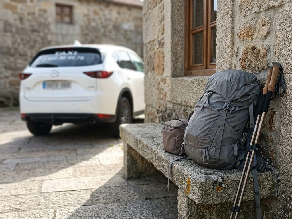 Mochila y bastones de senderismo en un banco de piedra junto al taxi, en la Ribeira Sacra
